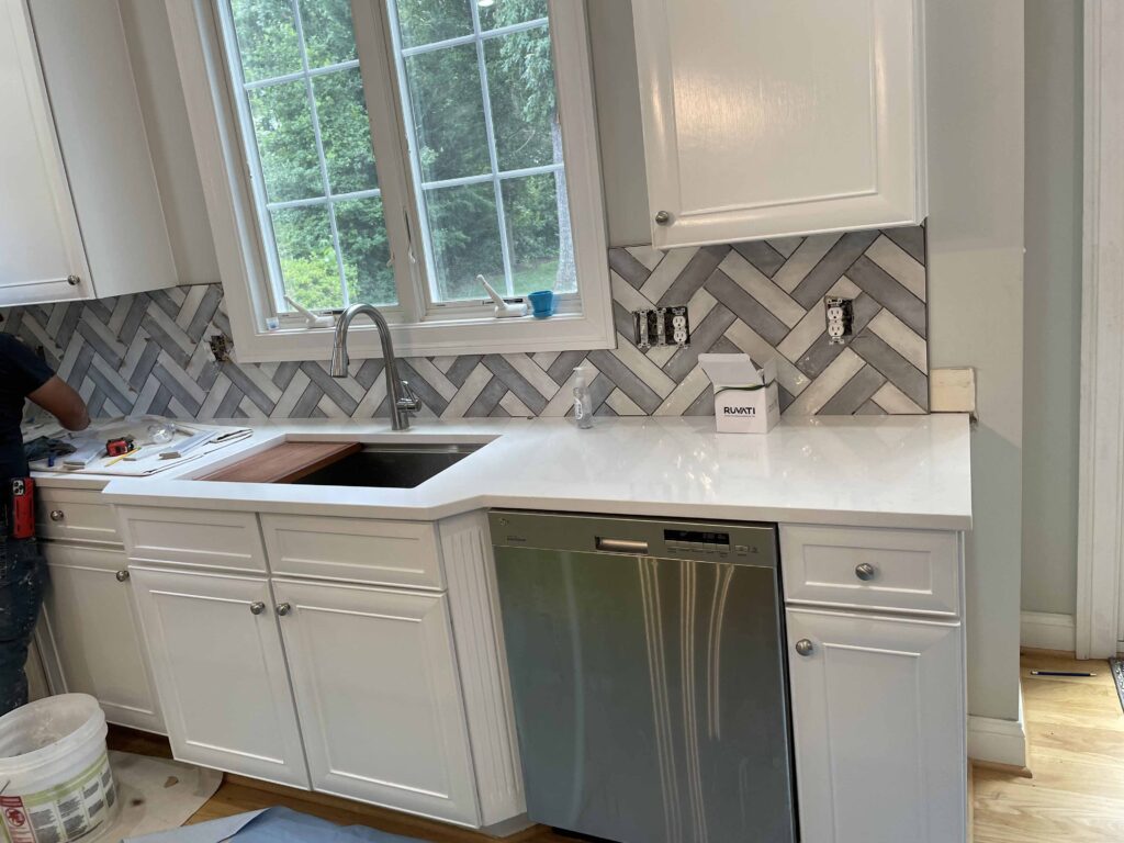 White kitchen cabinets and sink with a herringbone tile backsplash
